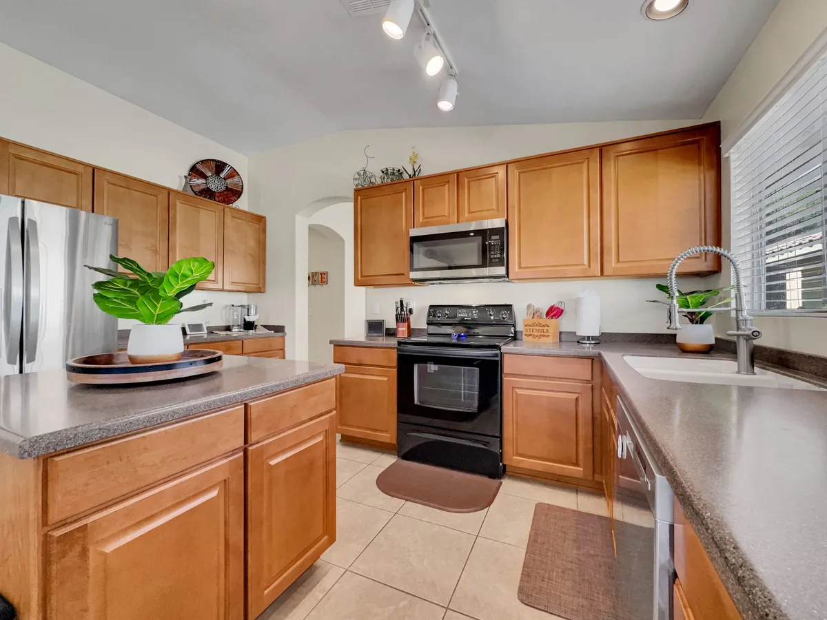 The image shows a warm, inviting kitchen with a spacious island, modern cabinetry, stainless steel appliances, and a touch of greenery. The setup is ideal for preparing family meals and coming together after a day exploring outdoors.