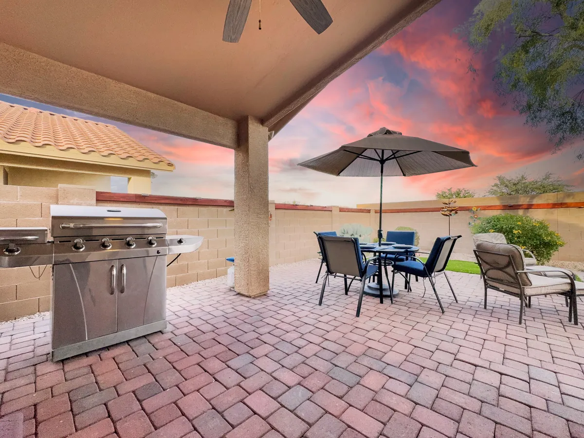 A cozy patio scene showcasing a grill, a dining table set under an umbrella, and inviting patio furniture. The sunset ambiance hints at memorable al fresco dinners and social BBQs.