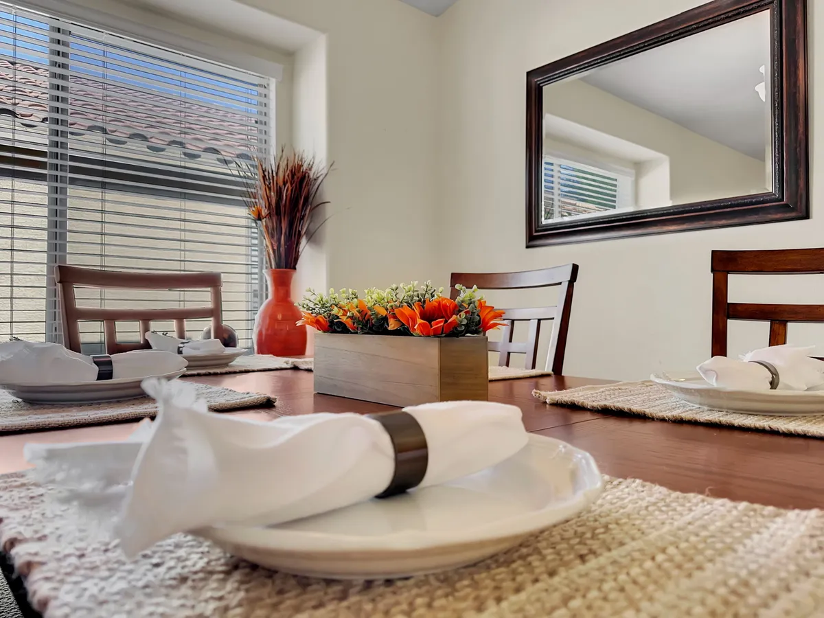 A welcoming dining area centered around a stylish table set with a decorative centerpiece. Soft natural light filters through window blinds, creating a cozy ambiance for family meals, dinner parties, or casual get-togethers.