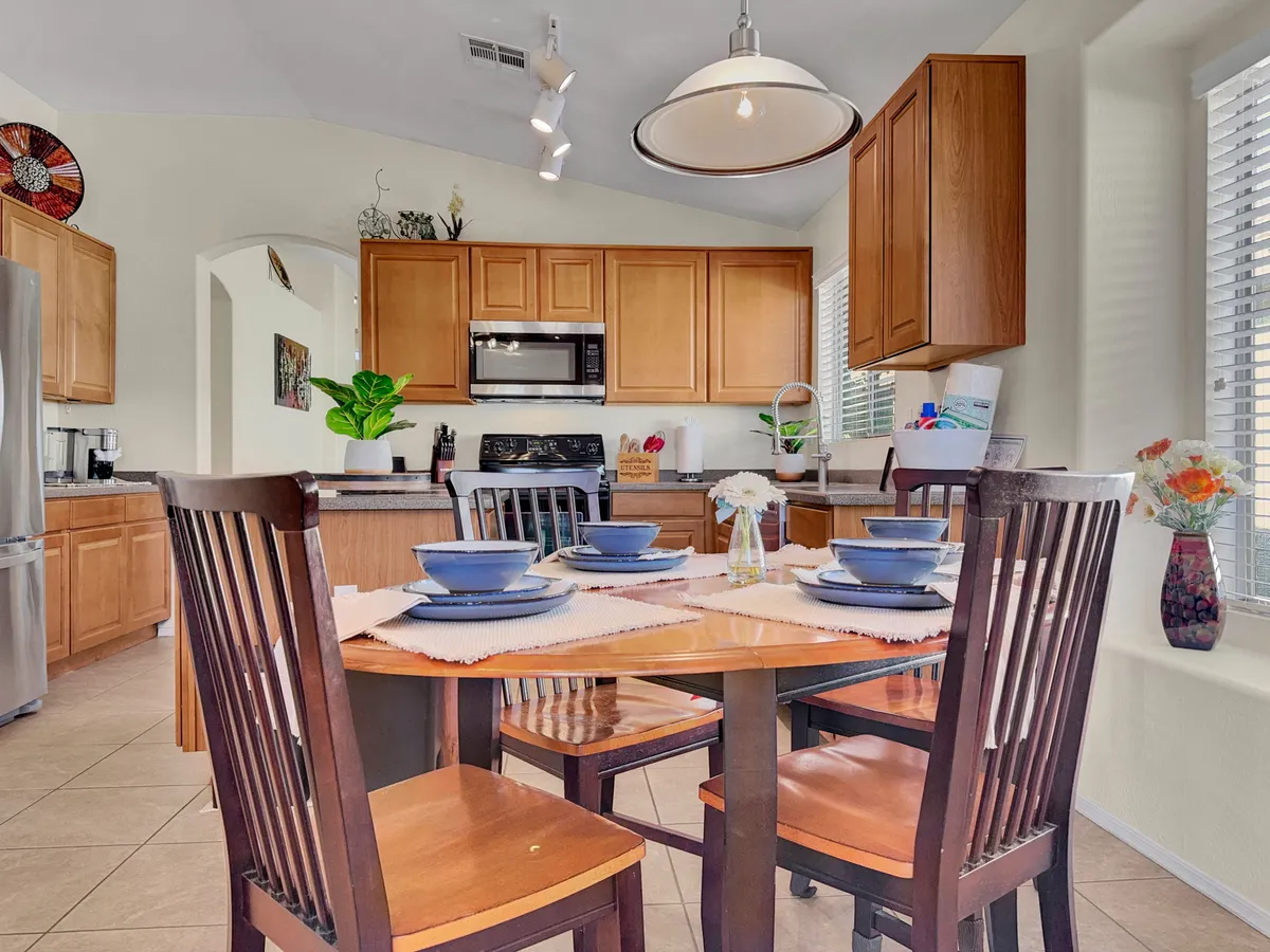 A welcoming dining area set for a meal, with kitchen cabinetry, decorative wall art, and lush plants visible. The setting suggests gatherings, shared meals, and a homelike ambiance ideal for guests staying a while.