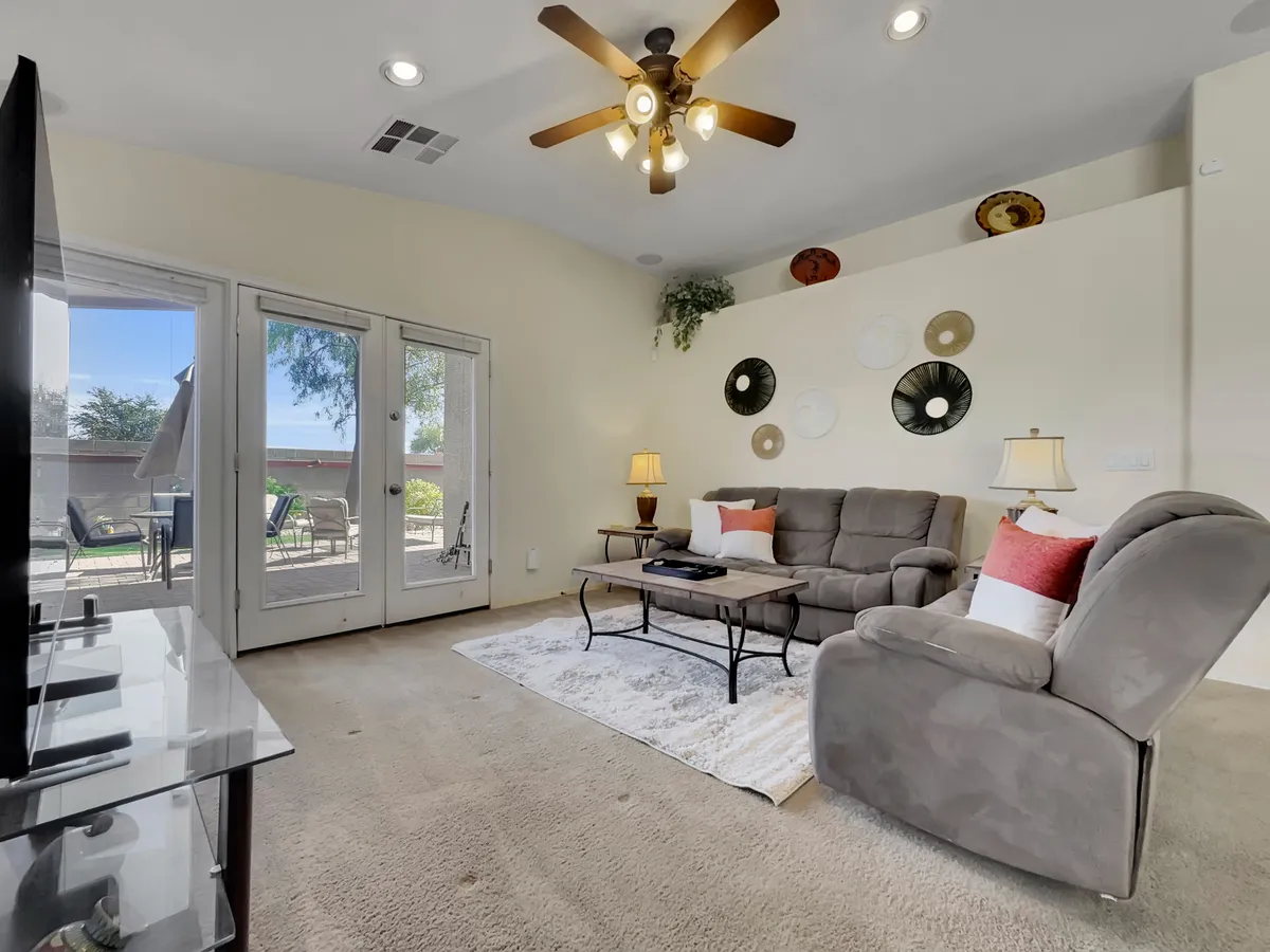 This image highlights a cozy living space with a comfortable sofa, coffee table, decorative plates on the wall, and sliding glass doors that likely lead out to a private garden or patio. The room feels intimate yet open to outdoor possibilities.