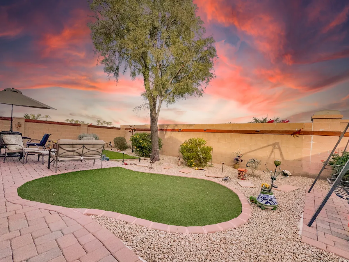 The backyard features artificial grass, a mature tree, patio furniture arranged for relaxation, and a serene sunset sky. The space is ideal for unwinding after a day outdoors, hosting family gatherings, or enjoying quiet moments in nature.