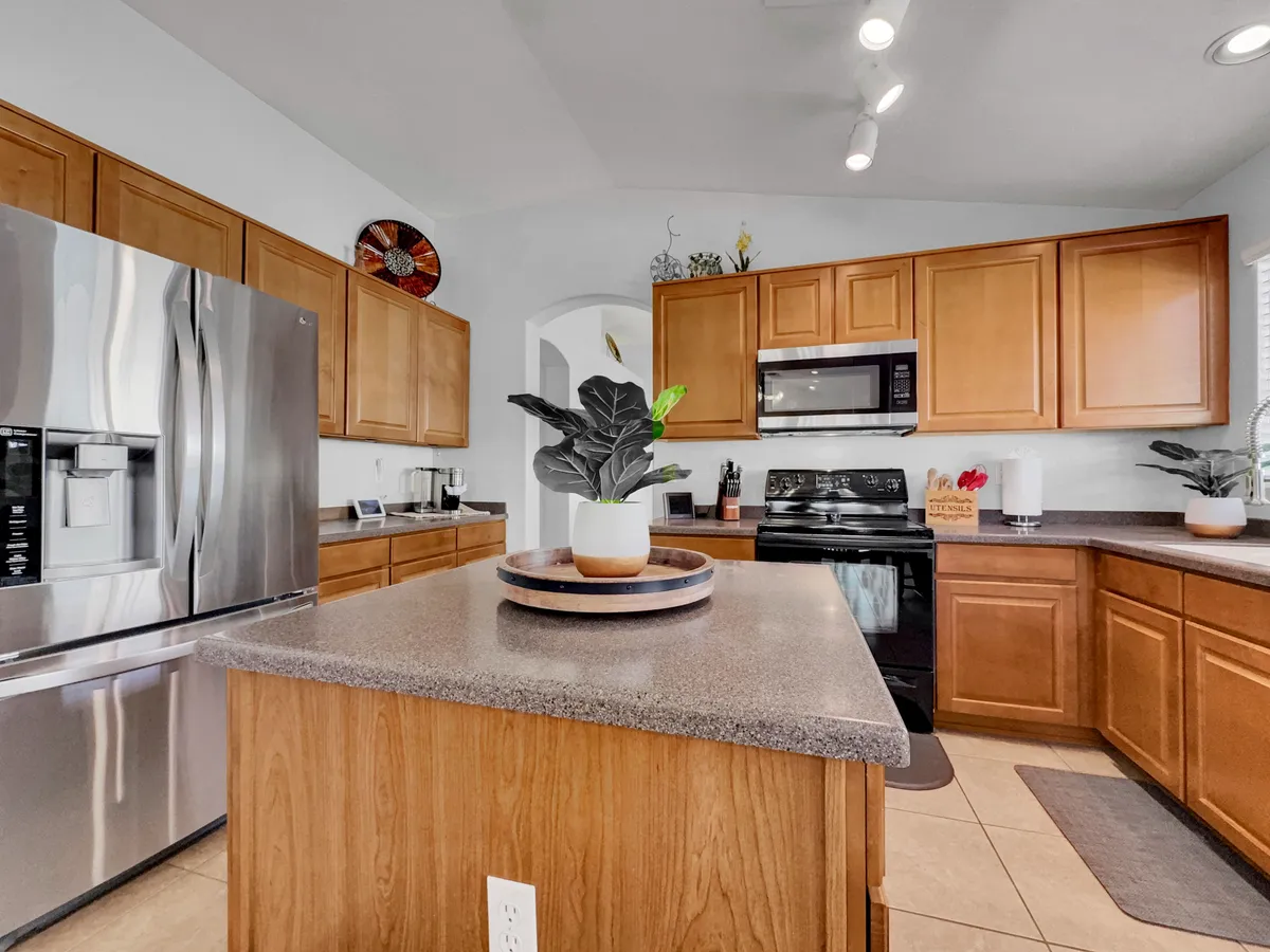 A modern, fully equipped kitchen featuring a spacious kitchen island, stainless steel appliances, warm wooden cabinets, and touches of greenery. The space is arranged to facilitate cooking, entertaining, and gathering, with ample surface area for meal preparation and socializing.