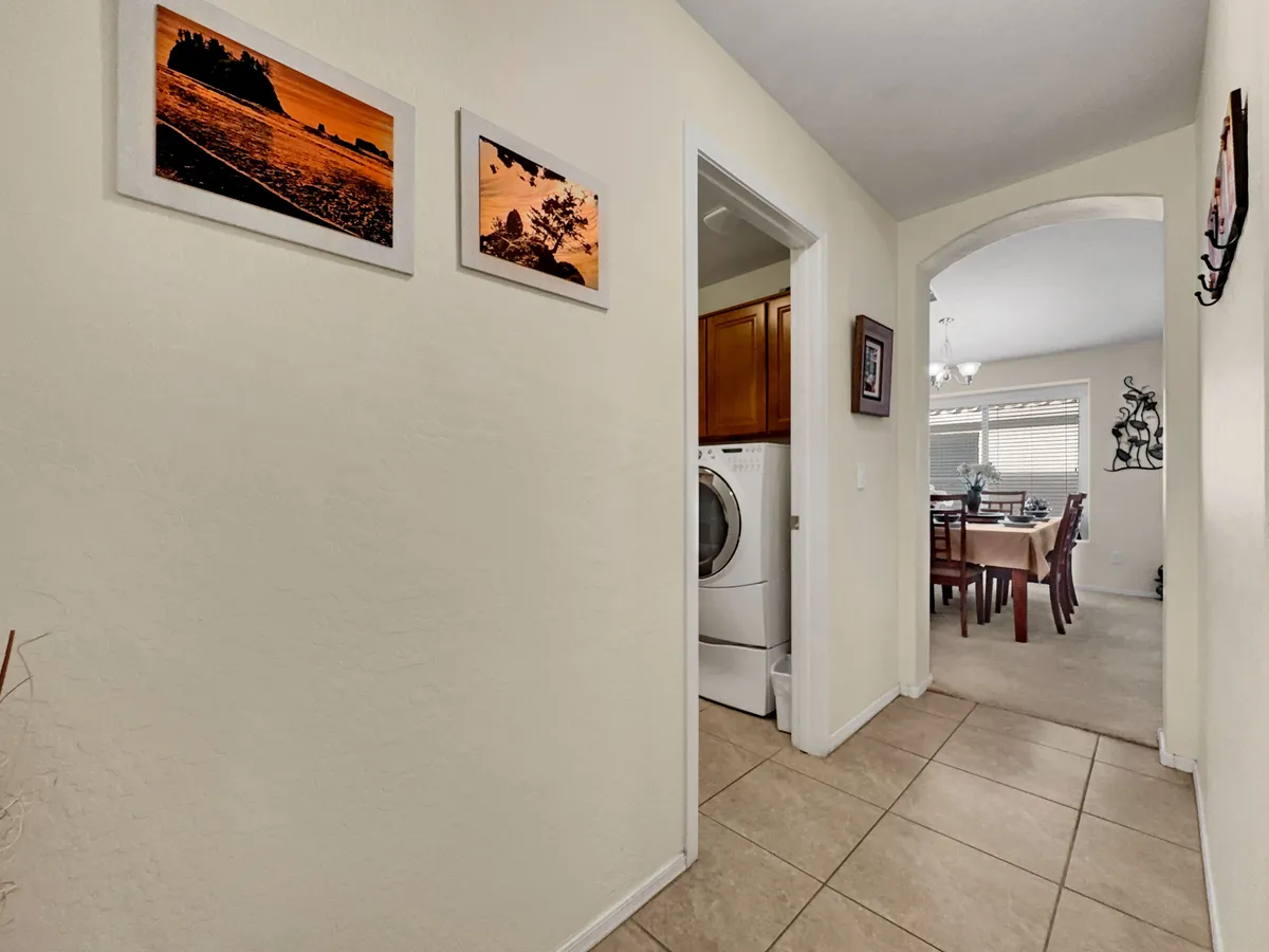 This image shows a cozy hallway featuring a washer and dryer, framed artwork on the wall, and a glimpse into a warm living area. The laundry appliances are integrated into the living space, enhancing convenience for long-term guests.